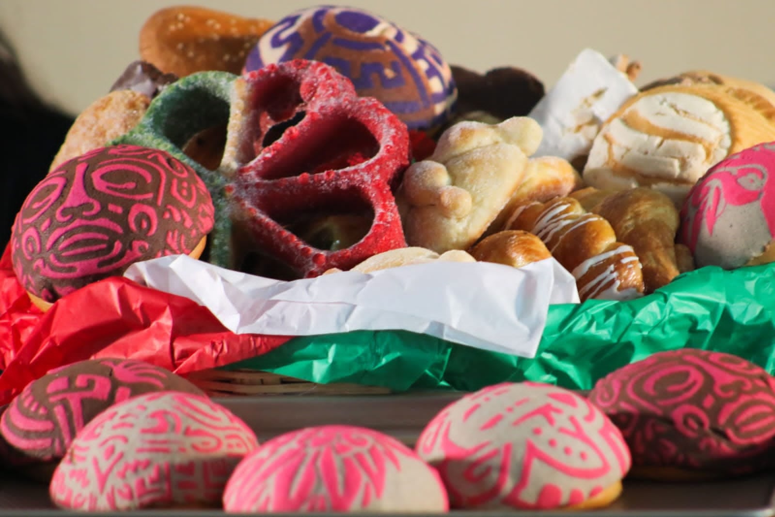Una variedad de galletas de azúcar decoradas con motivos de colores y piezas de pan dulce reposan en un recipiente adornado con papeles de colores. (Festival del Pan/Secretaría de cultura CDMX)