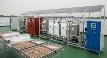 Laboratorio con paneles solares, equipo de electrolisis, bolsas de hidrógeno, bandejas con cáscaras de camarón trituradas y recipientes con carbonato de calcio.