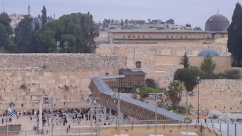 Vista aérea del Muro de las Lamentaciones en Jerusalén con personas abajo, una rampa de madera, y edificios históricos como la Cúpula de la Roca al fondo