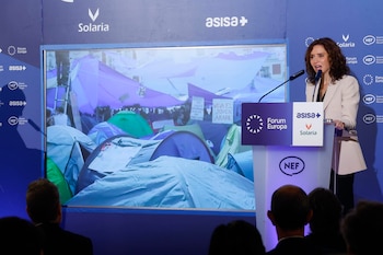 Isabel Díaz Ayuso durante un desayuno informativo de Nueva Economía Fórum. En la pantalla, la acampada por la vivienda en la Puerta del Sol.