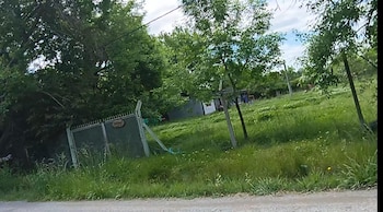 Portón metálico con malla verde y cartel de Quinta Sampi, rodeado de vegetación y árboles bajo un cielo parcialmente nublado