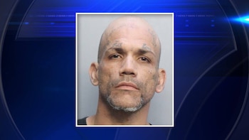 Primer plano de un hombre calvo con barba gris, tatuajes en la frente y mejillas, y expresión seria, sobre un fondo policial