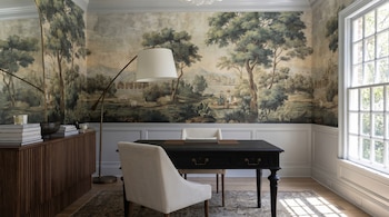 Oficina con tapiz mural de paisaje pastoral, escritorio negro con sillas beige, lámpara de pie y ventanal con vista a árboles.