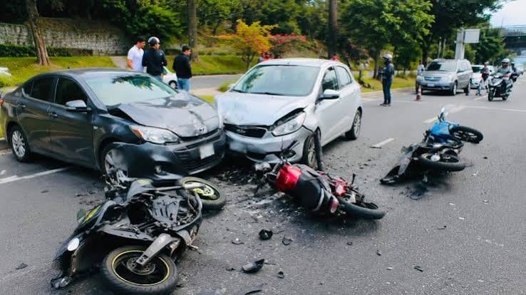 Dos automóviles y tres motocicletas se encuentran involucrados en una colisión en una vía pavimentada, mientras varias personas observan el lugar del incidente. (Redes Sociales)