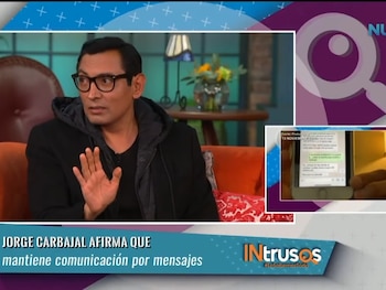 Jorge Carbajal, con gafas y chaqueta negra, gesticula en un set de televisión. Una pantalla auxiliar muestra un celular con mensajes de texto