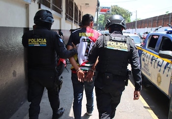 Dos policías con casco y chaleco sostienen a un hombre esposado que viste una camiseta con el nombre Ronaldo en una calle
