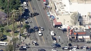 Vista aérea de una intersección con múltiples vehículos y agentes de policía en la calle, cinta amarilla, coches detenidos, palmeras y edificios