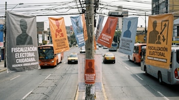 Carteles coloridos con siluetas humanas y el texto Fiscalización Electoral Ciudadana cuelgan de cables en una calle con autobuses.