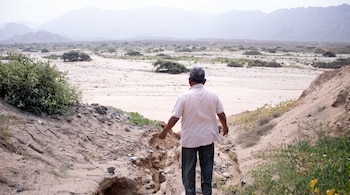 Vista posterior de un hombre en un zanjón de arena que mira hacia un llano árido con montañas al fondo.