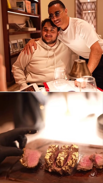 Un hombre sonriente con barba es abrazado por el chef Salt Bae en un restaurante, mientras una mano con guante negro sirve un filete con láminas de oro
