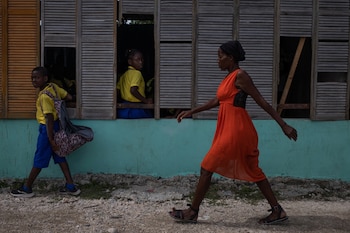 Una mujer pasa caminando mientras los niños esperan el transporte en la Escuela Santa María de la Familia Kizito situada en el barrio de chabolas de Cite Soleil en Puerto Príncipe, Haití (Reuters)