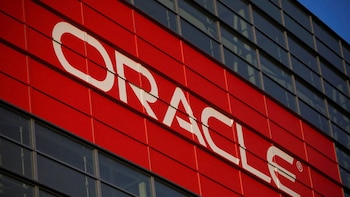 Primer plano de la fachada de un edificio corporativo con el logo blanco "ORACLE" sobre un panel rojo, y secciones de ventanas oscuras
