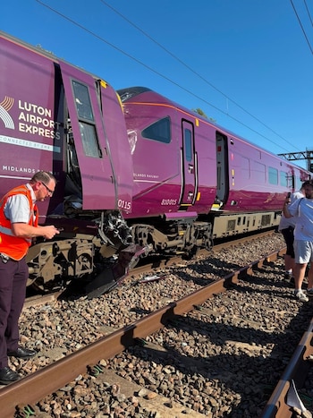 Tren de pasajeros morado con daños en el frontal detenido sobre vías de ferrocarril. Un trabajador con chaleco naranja observa el tren junto a otras personas