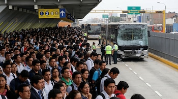 Gran multitud de personas espera en estación del Metropolitano. Un autobús con parabrisas roto y daños frontales está en la vía, con agentes policiales.