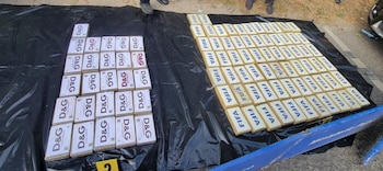 Cincuenta y cuatro paquetes rectangulares con el logotipo "D&G" y noventa y nueve paquetes con el logotipo "FIFA" sobre una lona negra. Se ven pies de personas