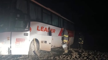 Vista nocturna de un colectivo blanco y rojo de la empresa Leader atascado en una banquina de tierra, con personal de rescate alrededor