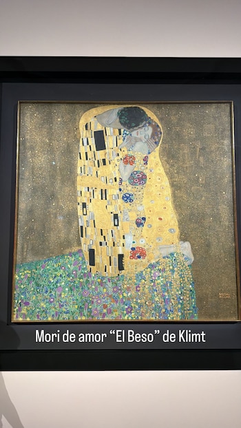 Una pintura enmarcada de 'El Beso' de Gustav Klimt, con una pareja abrazándose envuelta en túnicas doradas y ornamentos de mosaico sobre un fondo brillante