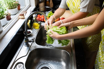 Personas lavando una lechuga debajo del grifo de la cocina. (Magnific)