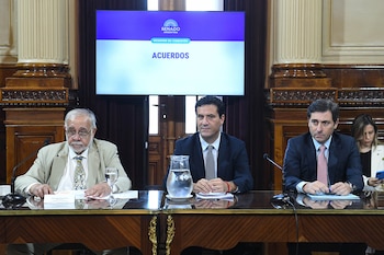 Tres hombres sentados en una mesa de madera pulida en una sala formal, con una pantalla grande detrás que muestra "SENADO ARGENTINA" y "ACUERDOS"