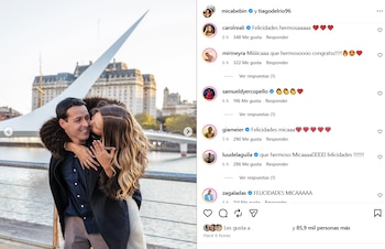Una mujer besa en la mejilla a un hombre mientras muestra un anillo de compromiso frente al puente de la Mujer