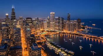 Vista aérea de Chicago al anochecer, mostrando un horizonte denso de rascacielos iluminados, un río con barcos y el vasto lago Michigan.