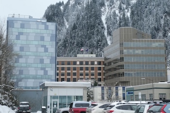 Vista invernal de edificios en Anchorage con montañas nevadas detrás, incluyendo un edificio de ladrillo con banderas y varios coches estacionados