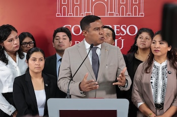 Un hombre de traje habla en un micrófono en un podio. Detrás, varias personas. Al fondo, pared roja con el texto "Congreso Perú" y un dibujo