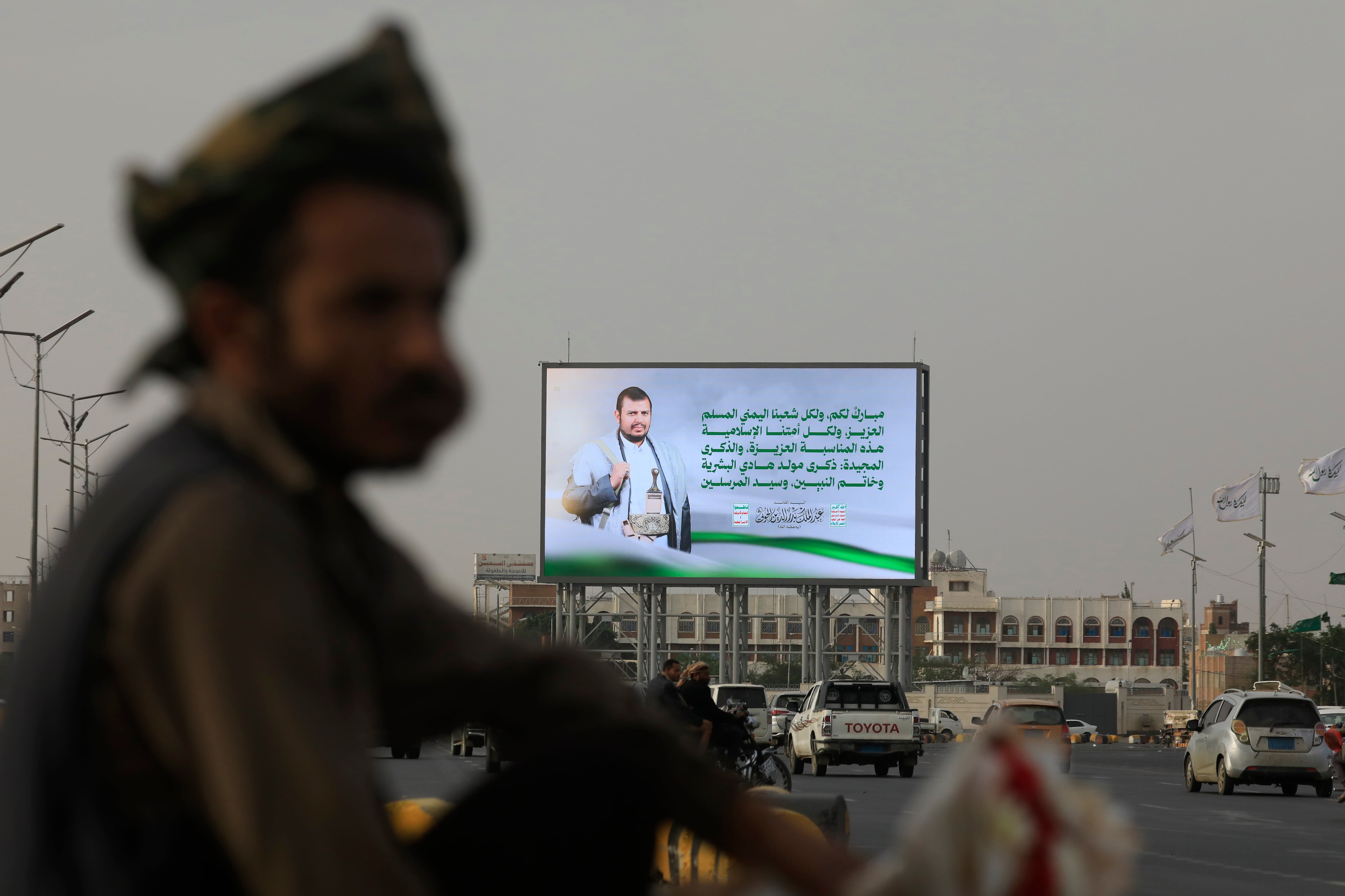 Vehículos fueron captados este 5 de septiembre al pasar ante una valla publicitaria digital en la que aparece el líder hutí Abdul-Malik al-Houthi, en una calle de Saná (Yemen). EFE/Yahya Arhab