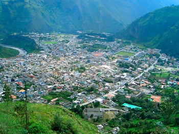 Vista aérea de Baños de Agua Santa, Ecuador, con edificaciones, un campo de fútbol y un río serpenteando en un valle montañoso verde