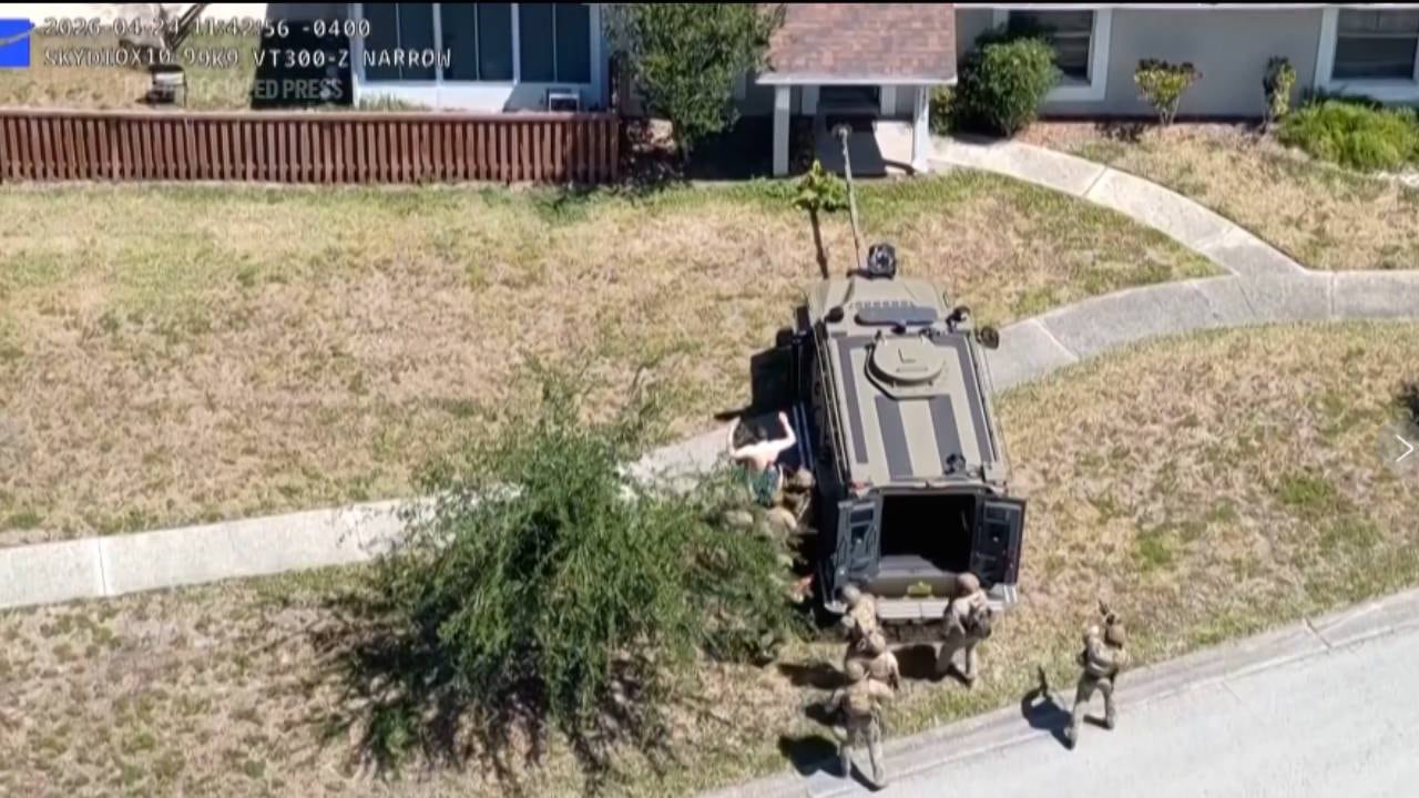 Un vehículo táctico blindado y personal de seguridad se despliegan durante una operación en una zona residencial, con una persona en el suelo cerca del vehículo (AP)