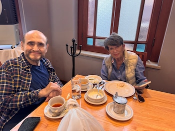 Edgar Vivar y Carmen Ochoa sentados sonriendo en una mesa de madera con tazas, platos con restos de comida y vasos en un restaurante