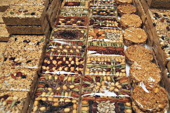 Múltiples barras rectangulares y discos circulares de cereales y frutos secos envueltos en plástico transparente, con semillas variadas