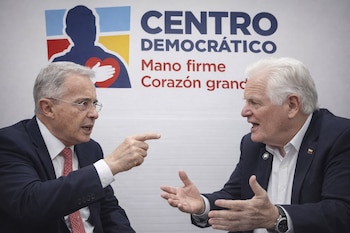 Dos hombres de edad avanzada, uno señalando y el otro gesticulando con las manos abiertas, discuten frente a un logo del Centro Democrático.