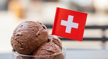 Vaso con varias bolas de helado de chocolate, una de ellas tiene insertada una pequeña bandera de Suiza roja con una cruz blanca.