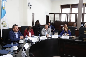 Personas sentadas ante micrófonos en una mesa en forma de herradura, bajo el emblema del Congreso de la República y banderas de Guatemala