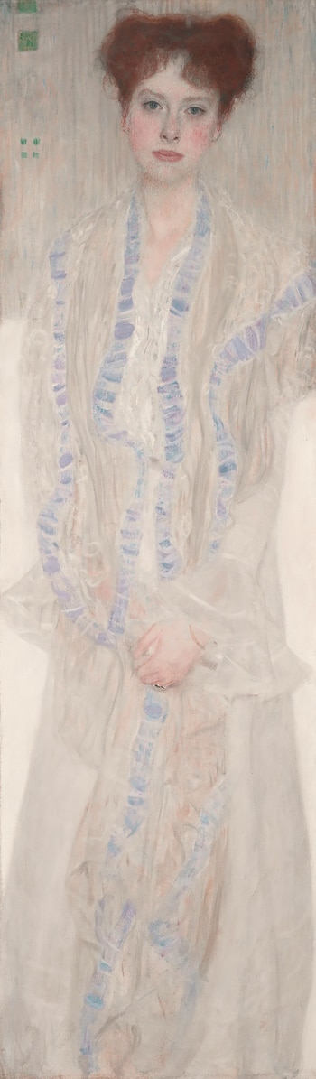 Pintura vertical de una mujer joven con cabello rojizo, tez pálida y ojos azules. Viste una prenda blanca translúcida con lazos azules y púrpuras. Las manos están unidas al frente