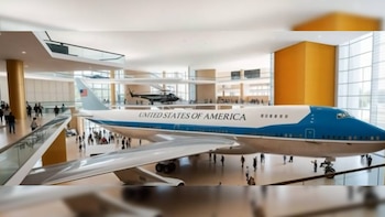 Una aeronave azul y blanca con las palabras "UNITED STATES OF AMERICA" en el costado, exhibida en un museo moderno con balcones y mucha gente
