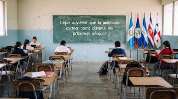 Un aula con paredes descoloridas, una pizarra verde con texto, seis estudiantes sentados en pupitres y banderas de Guatemala, Belice, Nicaragua, Costa Rica y Panamá.