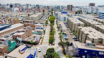 Vista aérea de una ciudad con edificios de múltiples pisos, una avenida central con árboles, calles con vehículos estacionados y algunos peatones