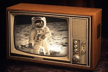 Un televisor antiguo con carcasa de madera muestra una imagen en blanco y negro de un astronauta de pie sobre la superficie lunar rocosa.