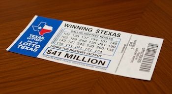 Primer plano de un boleto de la lotería Texas Lottery en color blanco y azul sobre una mesa de madera oscura, mostrando un premio mayor de $41 millones.