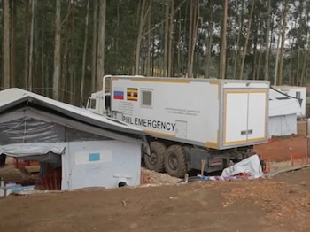 Camión blanco de laboratorio con las banderas de Rusia y Uganda aparcado junto a varias tiendas de campaña frente a un bosque