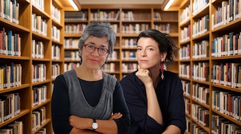Dos mujeres posan en primer plano frente a estanterías de madera llenas de libros en una biblioteca.