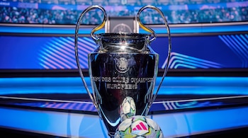 Trofeo de plata de la Liga de Campeones de la UEFA y balones de fútbol sobre una superficie en un escenario azul.