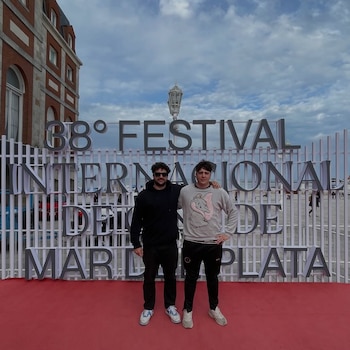Francisco Vignale y Lucas Vignale de pie en alfombra roja frente a cartel del "38° Festival Internacional de Mar del Plata". Edificio y cielo nublado al fondo