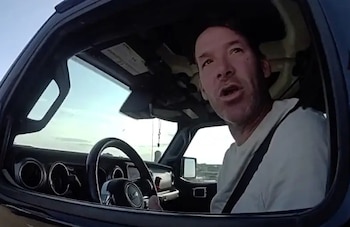 Un hombre con camiseta clara conduce un automóvil. Se observa su rostro, el volante del vehículo y parte del tablero