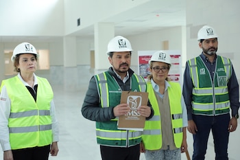 Cuatro personas, dos hombres y dos mujeres, con cascos blancos del IMSS y chalecos de seguridad, de pie en un espacio interior de construcción sin terminar
