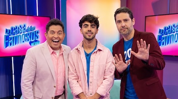 Tres hombres posan en un estudio de televisión. El de la izquierda viste un traje rosa claro. El del centro lleva una chaqueta de mezclilla rosa. El de la derecha un saco vino. Pantallas muestran el logo 'La Casa de los Famosos México'.
