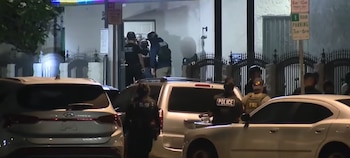 Agentes de Policía y del FBI con uniformes tácticos frente a un edificio con rejas y coches estacionados en la calle durante una operación nocturna