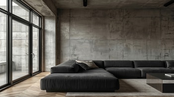 Salón contemporáneo con paredes de hormigón visto, un sofá modular en L de color gris oscuro, suelo de madera en espiga y grandes ventanales de suelo a techo.